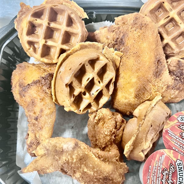 Southern fried chicken and waffles with syrup cups in a takeout container from C & E Southern Bites.