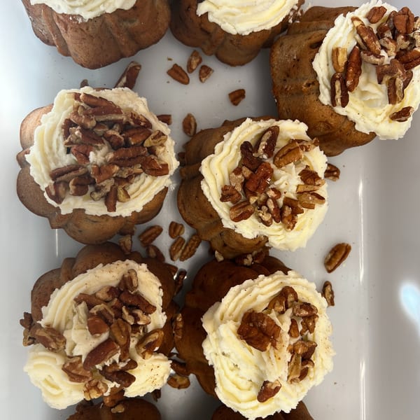 Pumpkin-shaped southern pecan cupcakes with creamy white frosting and chopped pecans on a white tray.