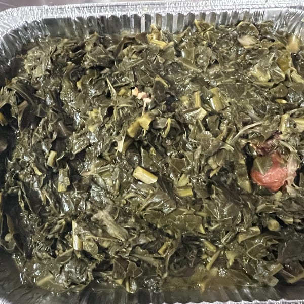 A close-up of C & E Southern Bites' collard greens with bits of meat in a foil pan.
