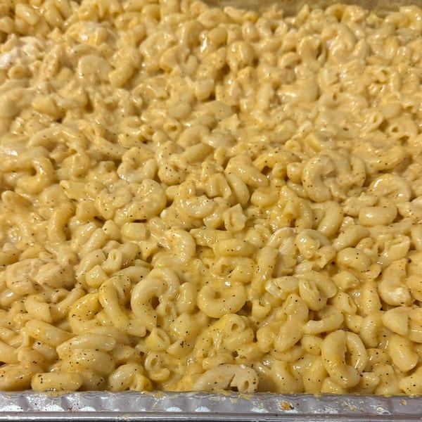 Close-up of creamy, golden macaroni and cheese with black pepper in a foil pan.
