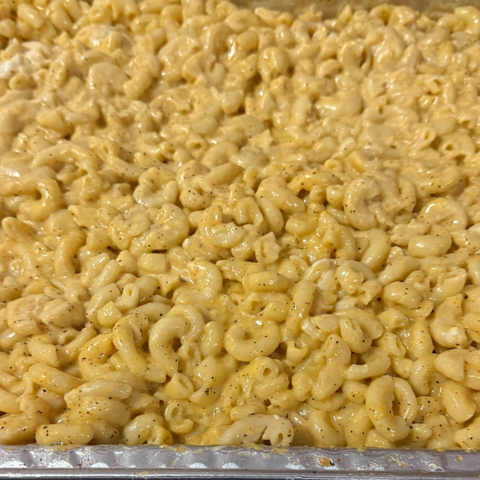 Close-up of creamy, golden macaroni and cheese with black pepper in a foil pan.