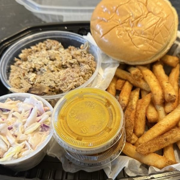 Southern pulled pork sandwich kit with fries, coleslaw, and sauce in a black takeout container.