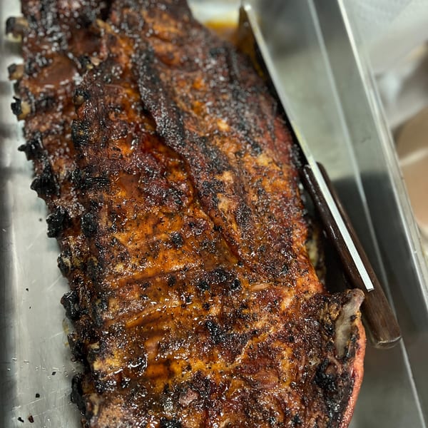 Close-up of a rack of C & E Southern Bites' BBQ ribs, glistening with sauce in a metal pan.