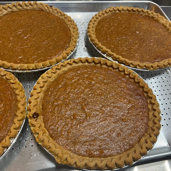 Four freshly baked sweet potato pies with crimped crusts on a metal baking sheet.