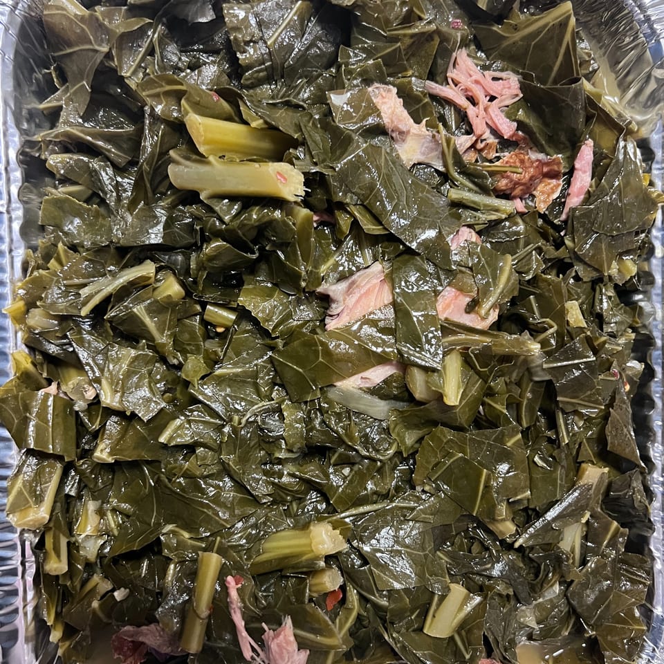 Close-up of southern collard greens with pieces of ham in a foil pan.