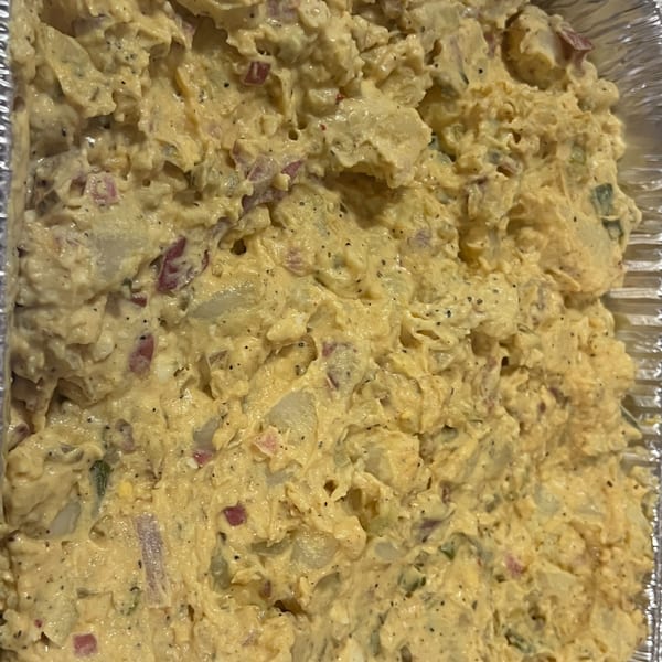 Close-up of creamy Southern potato salad with red onion and black pepper in a foil pan.