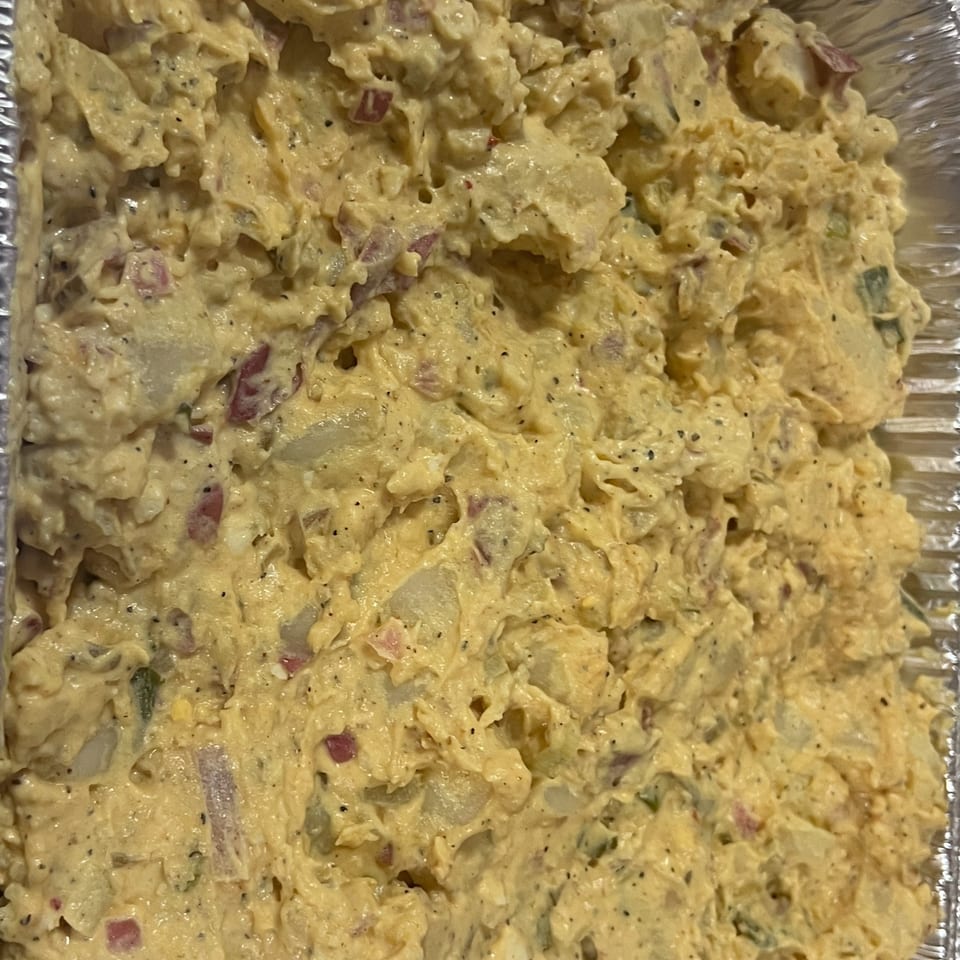 Close-up of creamy Southern potato salad with red onion and black pepper in a foil pan.
